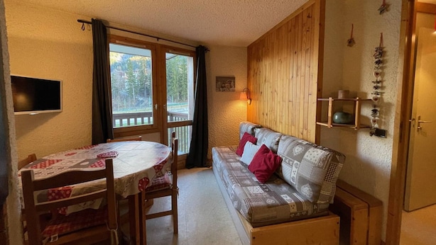 A cozy room with a dining table, a sofa, and a television mounted on the wall.