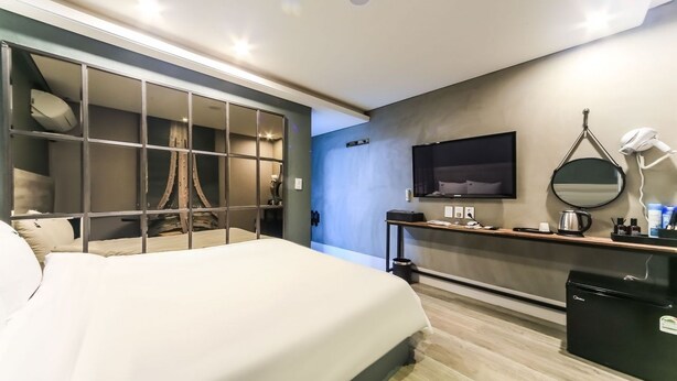 A modern bedroom with a bed, a vanity with a mirror, a television, and a desk. - Sol Motel (Busan)