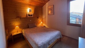 Ett mysigt sovrum med ett träpanelat tak, en säng, två sänglampor och ett fönster med utsikt över byggnaderna utanför.