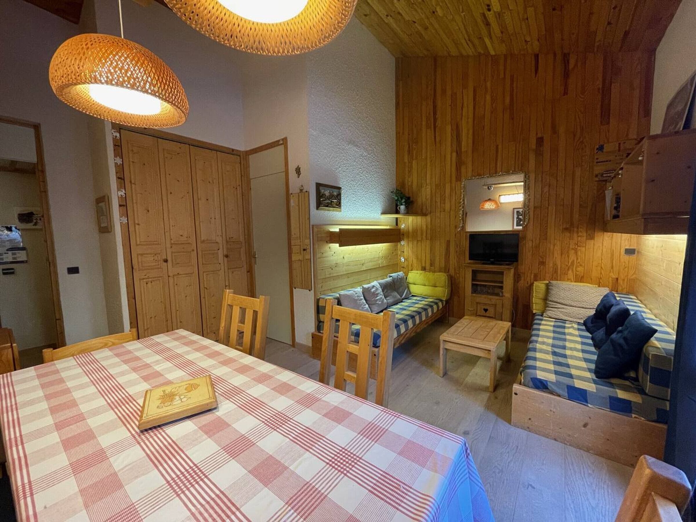 Een gezellige kamer met een geruit tafeltje, houten meubels, een bank en een televisie.