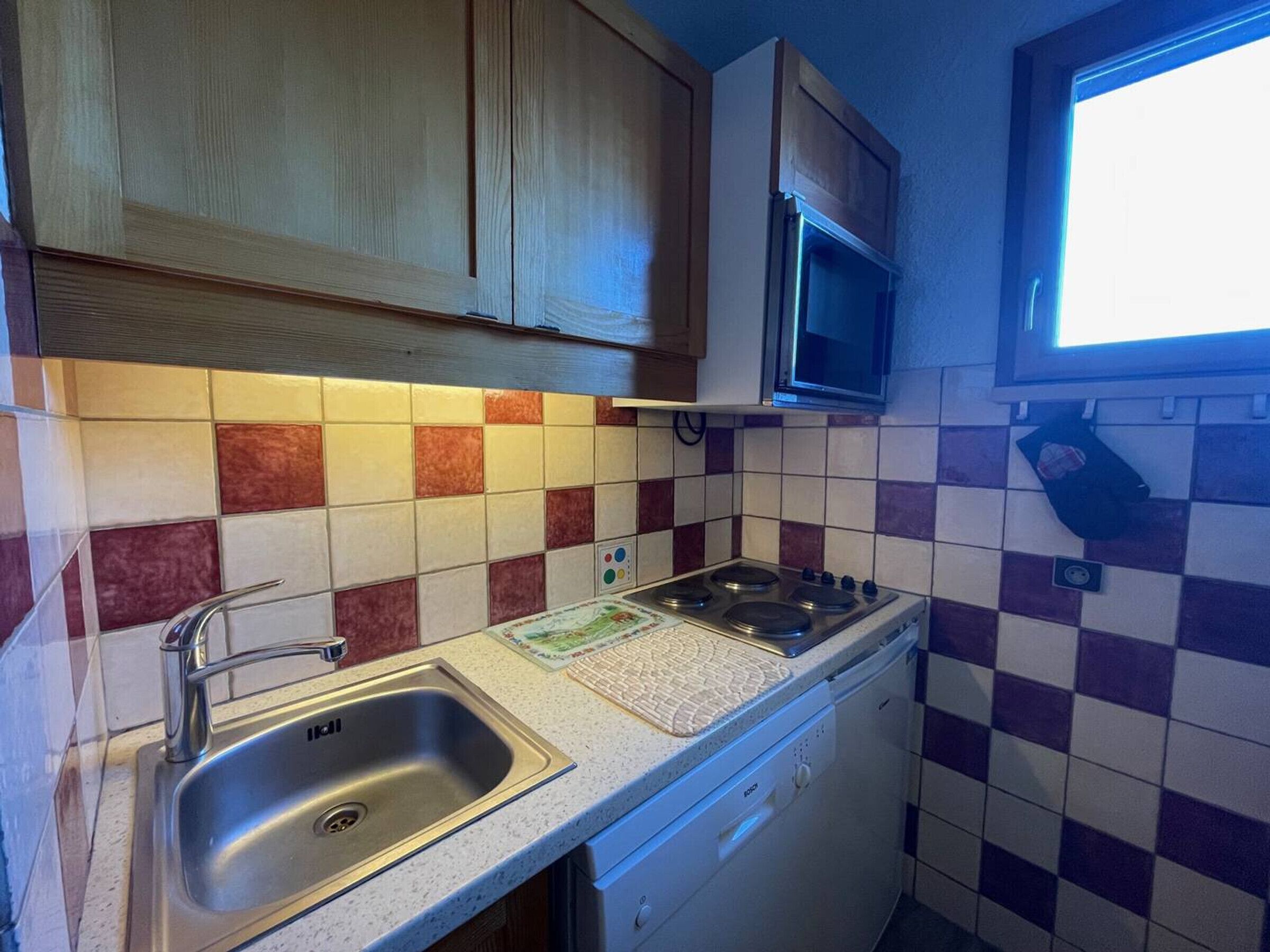 A kitchen with a stainless steel sink, a Bosch dishwasher, and a microwave above the stove.