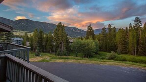 A mountain landscape with a clear sky and a wooden deck overlooking a road. - Condo w/beautiful views, fireplace & community pool/hot tub - Cozy Hidden Village Retreat (Big Sky)