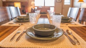 A dining table set with plates, bowls, cutlery, and glasses, with a television and windows in the background. - Condo w/beautiful views, fireplace & community pool/hot tub - Cozy Hidden Village Retreat (Big Sky)