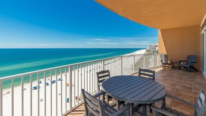 A balcony with a view of a beach and ocean, featuring a table and chairs. - 4 Bedroom Gulf Front Phoenix Orange Beach 806 (Orange Beach)