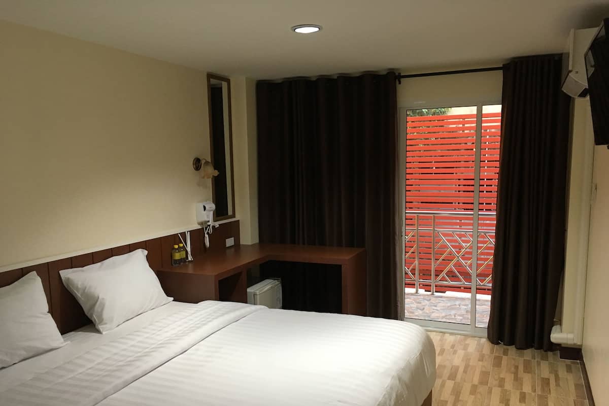 A hotel room with a bed, a desk, a mirror, a hairdryer, and a window with a view of a red fence.