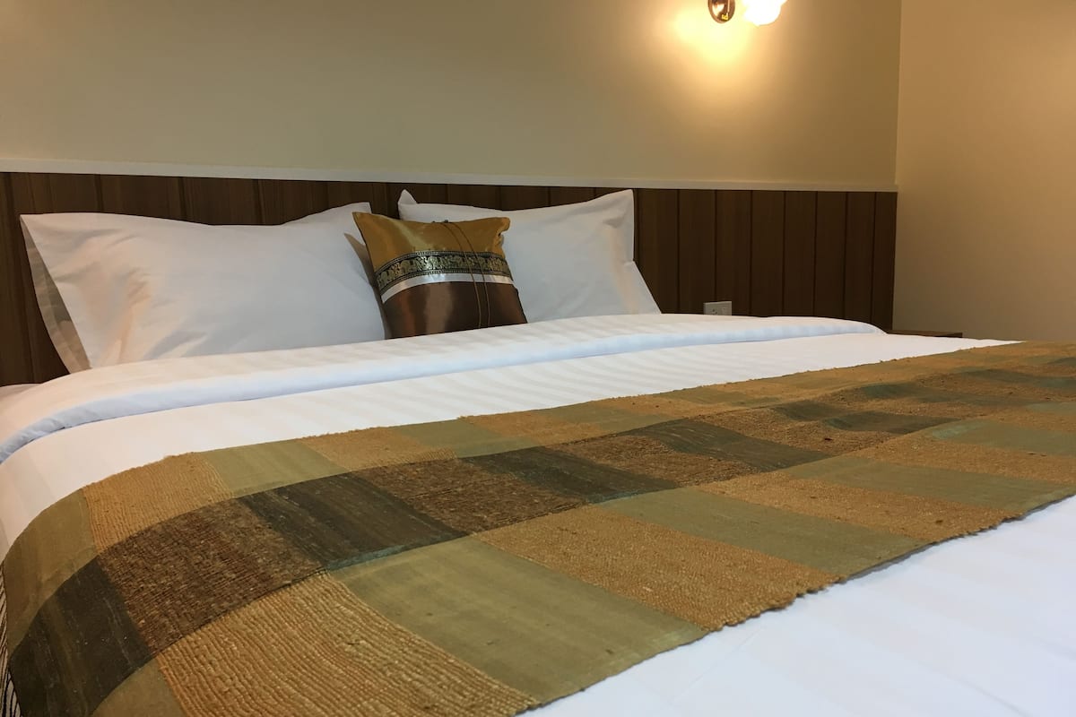 A neatly made bed with a checkered bedspread, white pillows, and a decorative pillow with a gold trim.