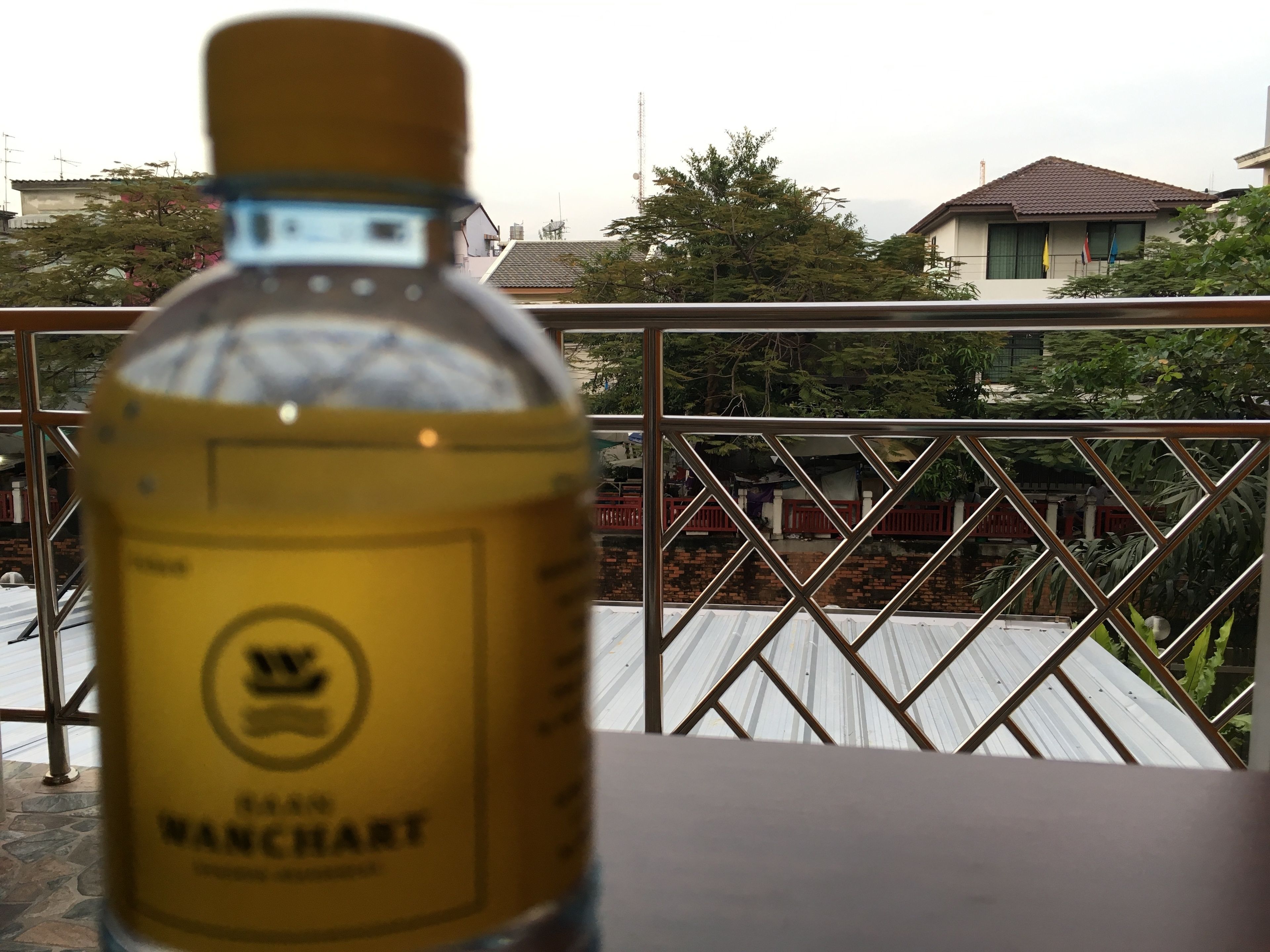 A bottle of Vanchart whiskey on a balcony with a view of residential buildings and trees.
