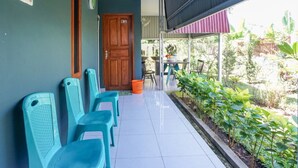 A corridor with turquoise chairs, a wooden door, and a view of a garden with plants and a table outside. - Rumah Kost MAPLE Winangun (Manado)