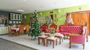 A living room with a Christmas tree, red sofas, and a dining area with wooden furniture. - Rumah Kost MAPLE Winangun (Manado)