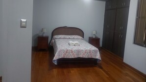 Un dormitorio con una cama, dos mesitas de noche con lámparas, un armario y una lámpara en el techo.