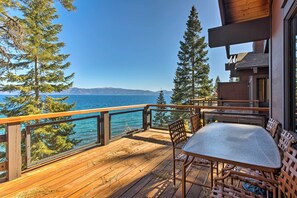 Eine Holzterrasse mit Tisch und Stühlen mit Blick auf einen See und Berge.