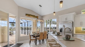 A modern kitchen with a large island, white cabinetry, and a view of the outdoors. - Gulf Access, Southern Heated Pool, Kayaks, Bikes, Tiki Hut - Villa Salty Shoreline - Roelens (Cape Coral)
