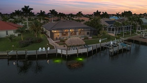 A waterfront property with a house, a dock, and a thatched-roof structure. - Gulf Access, Southern Heated Pool, Kayaks, Bikes, Tiki Hut - Villa Salty Shoreline - Roelens (Cape Coral)