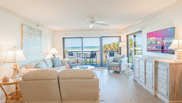 A spacious living room with a large TV, comfortable seating, and a balcony with a view of the ocean. - Direct oceanfront 2/2 condo with a large balcony, heated pool, and New Smyrna Beach access (New Smyrna Beach)