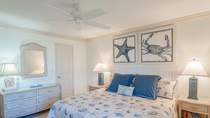 A bedroom with a bed, two nightstands, a dresser, a ceiling fan, and wall art. - Direct oceanfront 2/2 condo with a large balcony, heated pool, and New Smyrna Beach access (New Smyrna Beach)