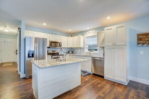 A modern kitchen with white cabinetry, a stainless steel refrigerator, a built-in microwave, and a granite countertop island. - Beach Blessing by Seaside Vacations & Sales (Chincoteague Island)