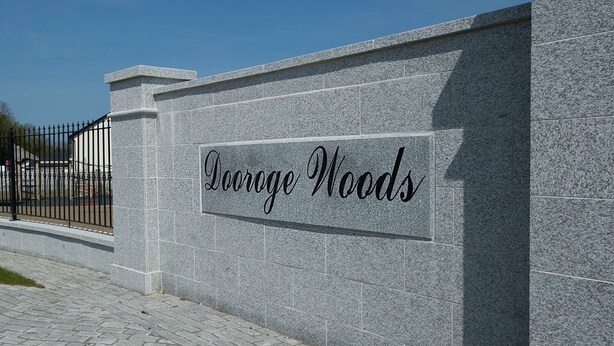 A stone wall with the inscription "Doorge Woods" on a paved walkway.