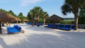 Une plage bordée de rangées de chaises longues bleues et d’ombrelles en chaume.
