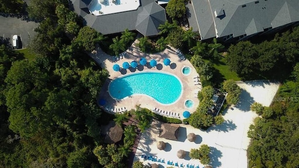 Vue aérienne d’un complexe hôtelier doté d’une grande piscine, entourée de chaises longues et de palmiers.