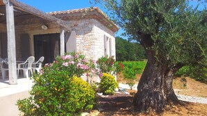 A rustic stone building with a tiled roof, outdoor seating, and a large tree.