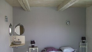 A bedroom with a bed, a bedside table with a lamp, a wall-mounted mirror, and a small shelf with a bowl.