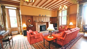 A cozy living room with a fireplace, red sofas, a wooden coffee table, and a plaid rug. - The Edwardian Wing, 18th Century Oak with Wing inserts (Taynuilt)