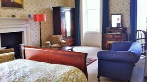 A traditional room with a bed, a blue armchair, a wooden cabinet, and a fireplace. - The Edwardian Wing, 18th Century Oak with Wing inserts (Taynuilt)