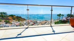 Een balkon met vrij uitzicht op zee, gebouwen en palmbomen.