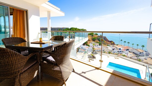 Een balkon met rieten meubilair, een glazen balustrade en uitzicht op een kustplaats en de oceaan.
