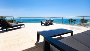 Een terras op het dak met lounge stoelen en een tafel, met uitzicht op een heldere blauwe zee.