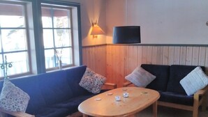 Une pièce avec un canapé bleu, une table basse en bois et un plancher en bois. Il y a une fenêtre avec des stores et une lampe fixée au mur.