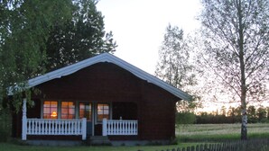 Une cabane rustique dotée d’un porche, entourée d’une clôture en bois et d’arbres.