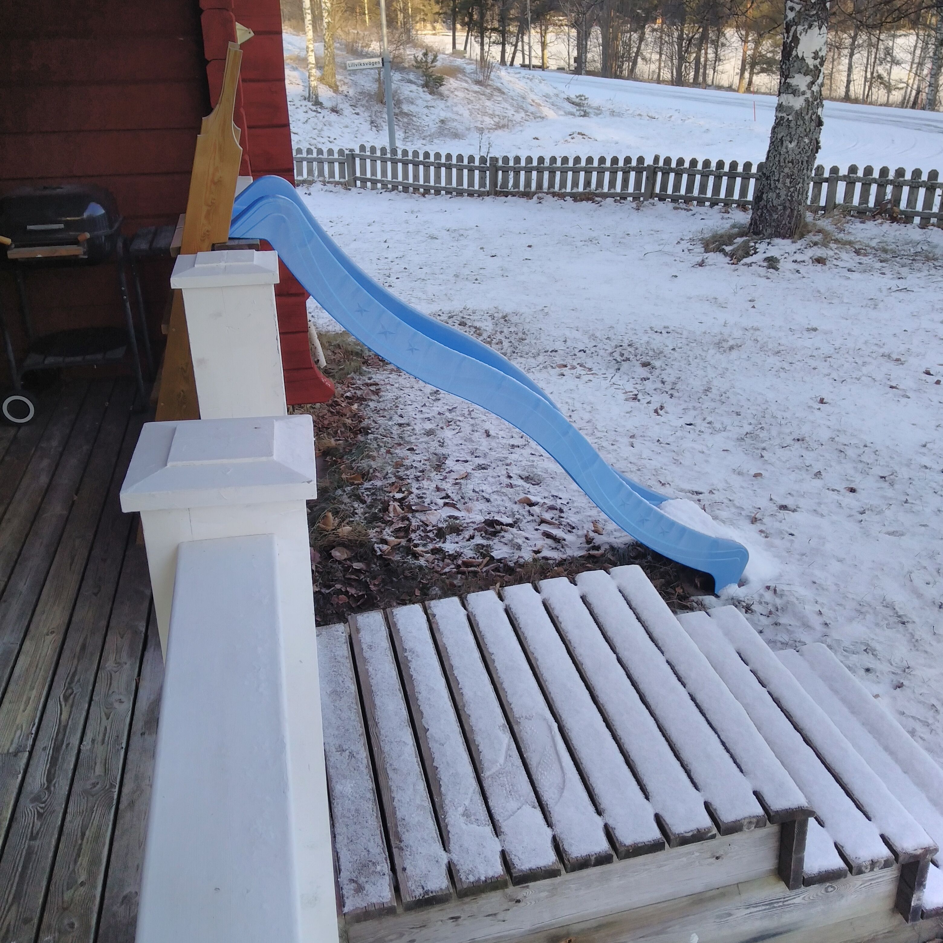 A wooden deck with a blue slide leading to a white bench.