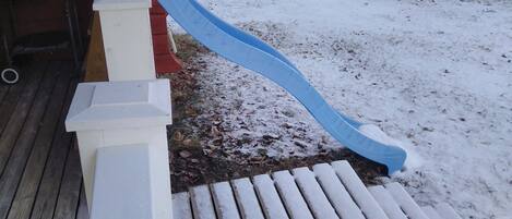 A wooden deck with a blue slide leading to a white bench.