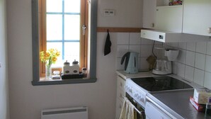 Une cuisine compacte avec une fenêtre, une cuisinière, une machine à café et une petite étagère.