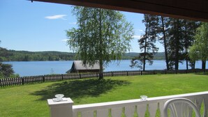 Une vue depuis une véranda donnant sur un lac, avec une clôture en bois et un petit bâtiment en arrière-plan.