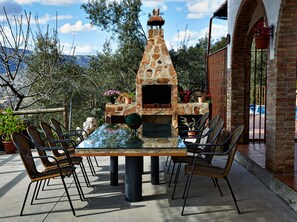 Un patio al aire libre con un horno de pizza de piedra, sillas de mimbre y una mesa con cubierta de vidrio.