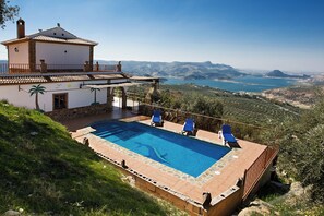 Una villa con piscina, sillas reclinables azules y vistas del paisaje circundante.
