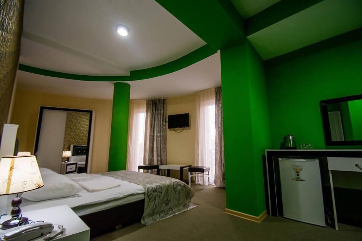 A hotel room with a bed, desk, and a small refrigerator.