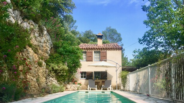 A poolside view of a house with a tiled roof, a stone wall, and a white fence.