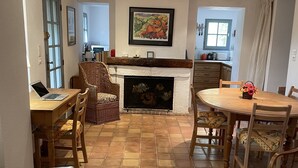 A cozy living room with a fireplace, a dining area with a table and chairs, and a laptop on a desk.