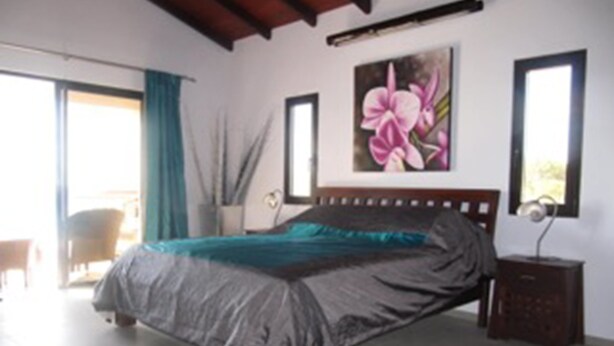 A bedroom with a bed, a nightstand, a painting, and a window. - De Luxe Duplex (The Valley)
