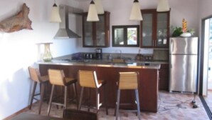 A modern kitchen with a central island, bar stools, pendant lights, and a refrigerator. - De Luxe Duplex (The Valley)