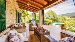 Un patio cubierto con mobiliario de mimbre, una piscina y vistas al campo.