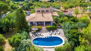 Una villa con piscina, rodeada de exuberante vegetación y vista a un paisaje urbano al fondo.