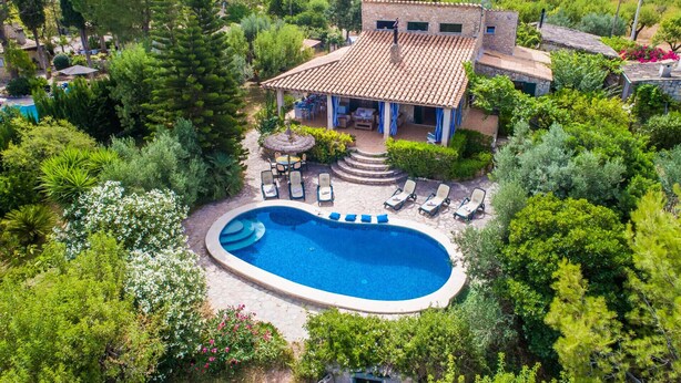 Vista aérea de una villa con piscina, rodeada de exuberante vegetación y un patio con techo de piedra.