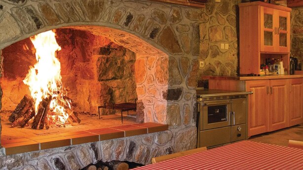 A stone fireplace with a fire, a kitchen area with cabinets, and a table with a checkered tablecloth. - 4 bedroom pet friendly home in Perusic (Perusic)