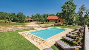 A rectangular swimming pool with a stone border, surrounded by a lawn and a stone wall. There are wooden lounge chairs with cushions along the pool's edge. - 4 bedroom pet friendly home in Perusic (Perusic)