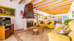 Un salón acogedor con chimenea, vigas de madera, un televisor y sofás amarillos.