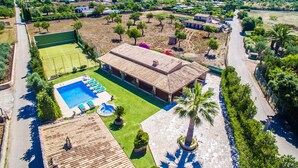 Vista aérea de una propiedad con piscina, cancha de tenis y un edificio grande con techo de tejas.